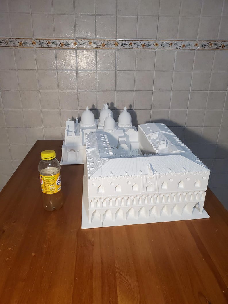 May include: A white 3D printed model of a building with multiple domes and a large courtyard. The model is sitting on a wooden table.