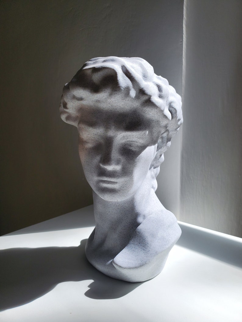 May include: White plaster bust sculpture of a person's head and shoulders. The sculpture has a textured surface and is in a minimalist style.