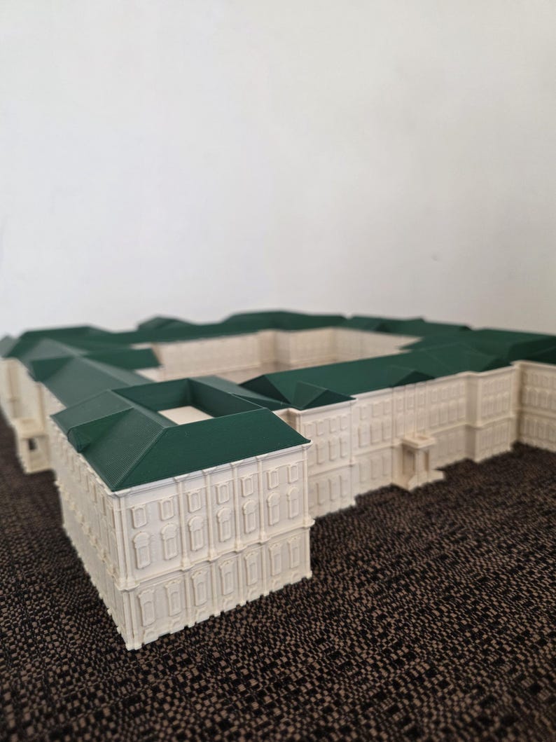 May include: A detailed architectural model of a building, featuring a cream-coloured facade and a green roof. The model showcases intricate window and door details, set against a neutral backdrop.