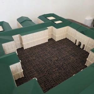 May include: A detailed miniature model of a building complex. The model features white walls, green roofs, and a central courtyard. The building has multiple windows and a detailed design.
