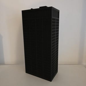 Peut inclure: Une maquette architecturale noire mate d'un gratte-ciel rectangulaire présentant une façade en forme de grille avec de nombreuses petites fenêtres carrées. La structure a un toit plat avec une petite section rectangulaire surélevée au sommet.