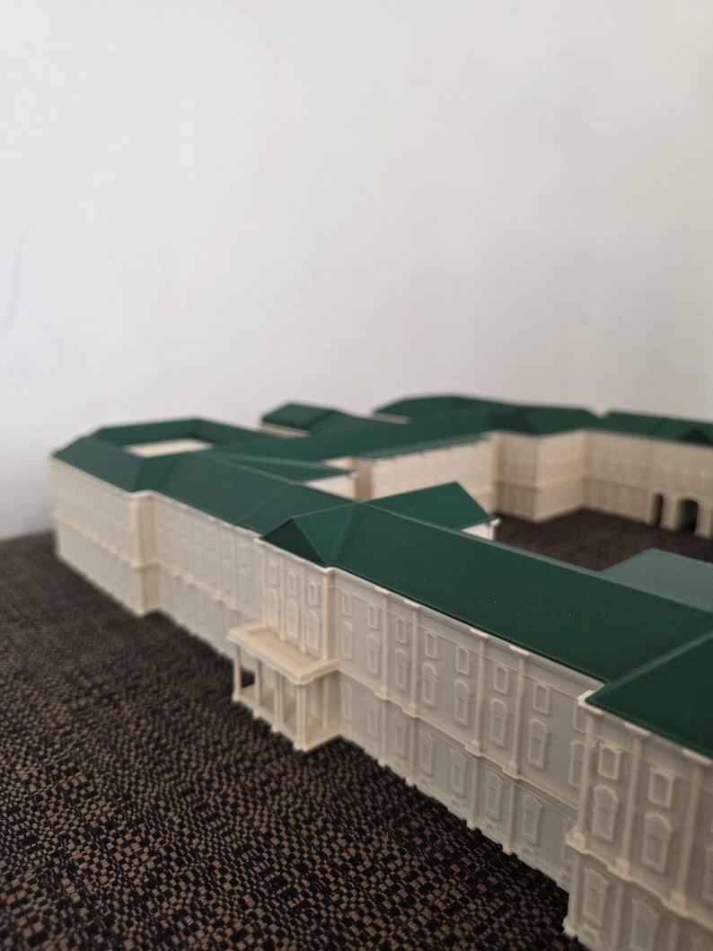 May include: A detailed architectural model of a building with a cream facade and a dark green roof. The model features intricate details, including windows and a small porch. The building is set against a plain background.