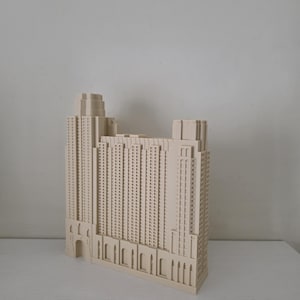 Peut inclure: Maquette architecturale beige d'un immeuble de grande hauteur. Le modèle présente des fenêtres détaillées, plusieurs niveaux et une forme rectangulaire. Le bâtiment a une tour au sommet et une série d'arches à la base. Le modèle est sur une surface blanche.