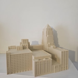 Peut inclure: Maquette architecturale beige d'un paysage urbain, avec des gratte-ciel et des bâtiments de faible hauteur. Le modèle est présenté sur une étagère blanche, sur fond blanc.