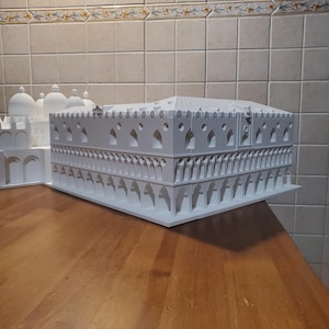 May include: A white 3D printed model of a building with intricate details and arches. The model is sitting on a wooden surface.