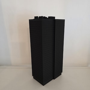 Peut inclure: Une maquette architecturale de gratte-ciel imprimée en 3D noir mat, présentant une structure rectangulaire avec une grille de petites fenêtres carrées couvrant les surfaces extérieures et un toit plat avec des saillies géométriques.