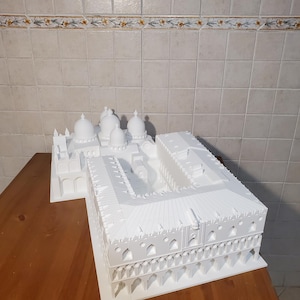 May include: White 3D printed model of a building with multiple domes and arches. The model is on a wooden surface.