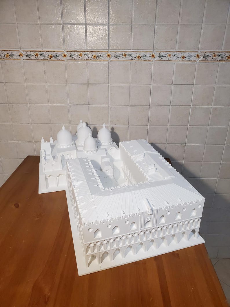 May include: White 3D printed model of a building with multiple domes and arches. The model is on a wooden surface.
