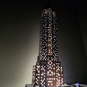 Puede incluir: Maqueta del Empire State Building con ventanas iluminadas. El modelo es marrón con muchas luces blancas cuadradas y brillantes que representan las ventanas del edificio. La iluminación interna crea un brillo cálido y acogedor.