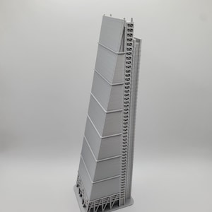 May include: A gray architectural model of a tall skyscraper with a unique, angled design. The building has a series of rectangular panels and a detailed support structure on one side. The model is set against a plain white background.