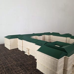 May include: A detailed architectural model of a building with a cream-coloured facade and a dark green roof. The model has multiple sections and appears to be a complex structure, possibly a palace or government building.