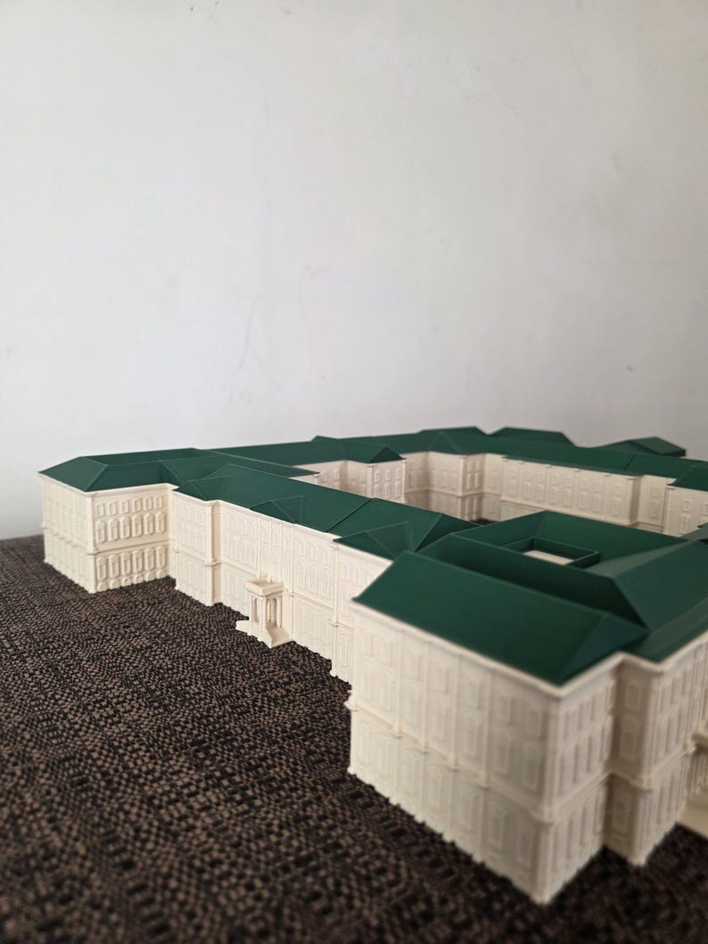 May include: A detailed architectural model of a building with a cream-coloured facade and a dark green roof. The model has multiple sections and appears to be a complex structure, possibly a palace or government building.