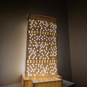 May include: A lit architectural model of the MetLife building. The model is made of a light-coloured material with numerous square windows that emit a warm glow. The MetLife logo is visible at the top.