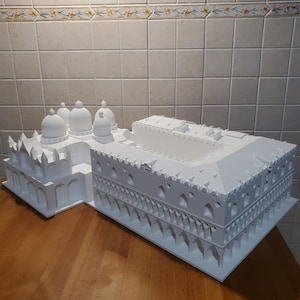 Op de afbeelding: Een wit 3D-geprint model van een gebouw met meerdere koepels en bogen. Het model staat op een houten oppervlak.