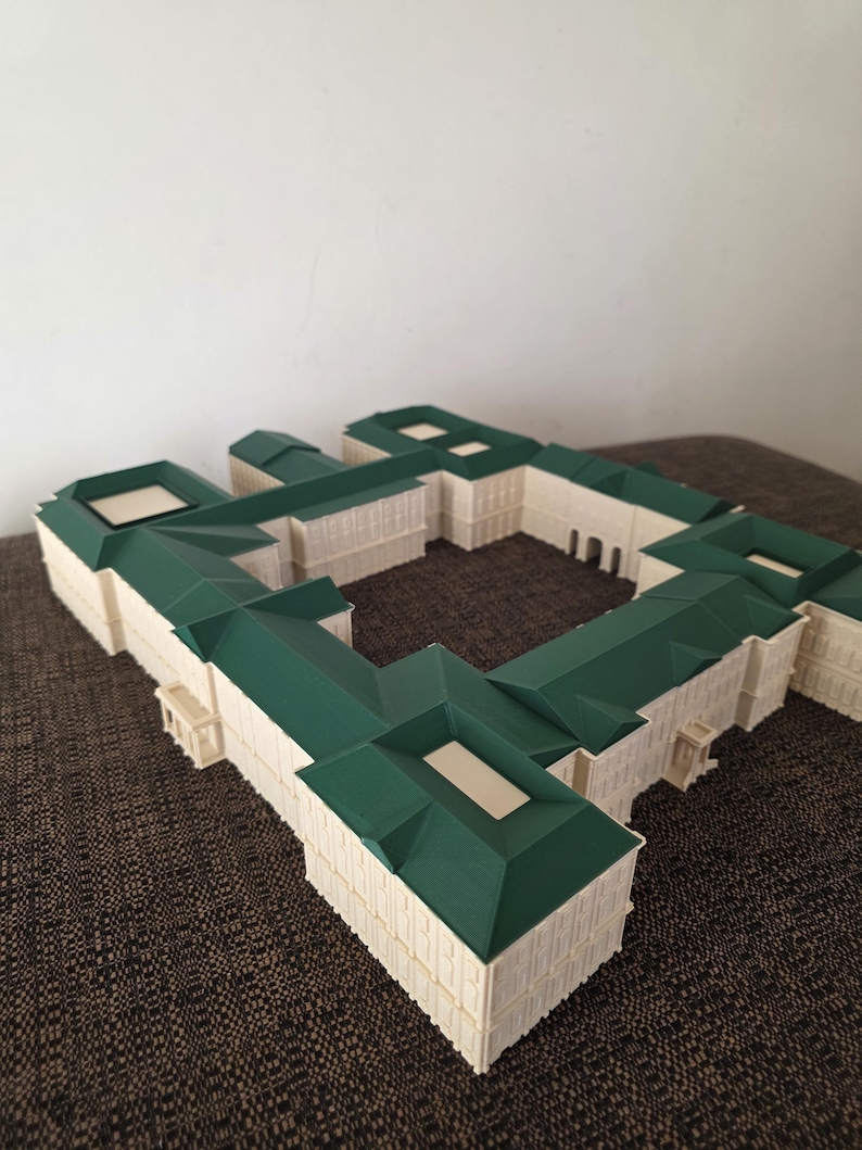 May include: A detailed architectural model of a building with a green roof and off-white walls. The model has a complex design with multiple sections and a courtyard. The roof is a dark green colour, and the walls are a light cream colour.