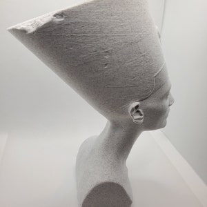 K&ouml;nnte beinhalten: Wei&szlig;e B&uuml;ste einer &auml;gyptischen K&ouml;nigin mit traditioneller Kopfbedeckung. Die Skulptur ist aus einem strukturierten Material gefertigt, das an Stein erinnert.