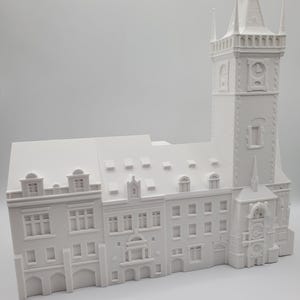 Puede incluir: Maqueta arquitectónica blanca de un edificio con una torre alta y varios pisos. El modelo tiene ventanas, tejados y elementos arquitectónicos detallados. El edificio es un monumento histórico.