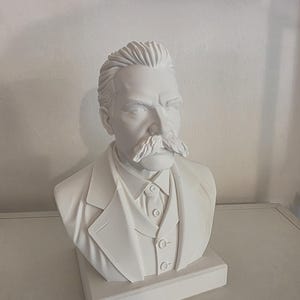 May include: A matte white bust sculpture depicting a person with a prominent moustache, styled hair, and wearing a collared shirt, waistcoat, and jacket. The figure is mounted on a rectangular base, capturing the head and shoulders in a neutral tone.