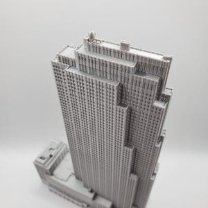 Könnte beinhalten: Graues Miniatur-Wolkenkratzer-Modell mit aufwendigen architektonischen Details. Das Gebäude verfügt über mehrere Ebenen, eine detaillierte Fassade und eine kleine Kuppel oben. Das Modell ist eine detaillierte Darstellung eines Hochhauses.