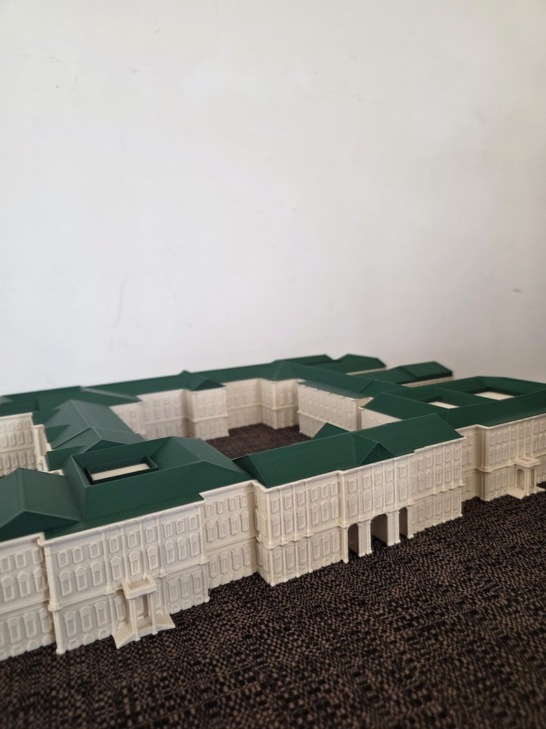 May include: A detailed architectural model of a building complex. The model features a cream-coloured facade with green rooftops. The design includes multiple rectangular structures with detailed window and door features.