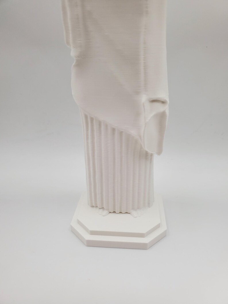 May include: White plaster statue of a woman standing on a square base with a fluted column. The statue is missing a portion of the drapery.