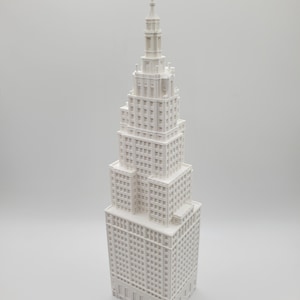 Peut inclure: Maquette architecturale blanche d'un gratte-ciel. Le bâtiment présente une façade détaillée avec de nombreuses fenêtres et une conception en gradins, culminant en une flèche. Le modèle est sur fond blanc.