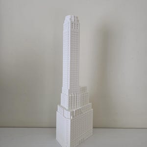 Può includere: Modello bianco di un grattacielo. Il modello presenta un design dettagliato con più livelli e una torre alta e snella. L'edificio ha un design a gradini ed è realizzato in un materiale bianco.