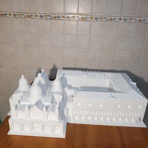 May include: A white 3D printed model of a building with multiple domes and arches. The model is on a wooden surface.