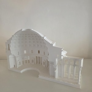 Puede incluir: Un modelo arquitectónico blanco impreso en 3D del Panteón, con una vista en sección transversal que revela la cúpula interior con su techo artesonado, nichos de pared circulares y el pórtico exterior con columnas sobre una base rectangular.