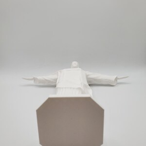 May include: White ceramic statue of Christ the Redeemer with outstretched arms, standing on an octagonal base.