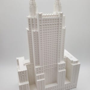 May include: A white architectural model of a skyscraper, featuring numerous levels, windows, and two spires. The model is a detailed miniature replica of a building, showcasing architectural features.
