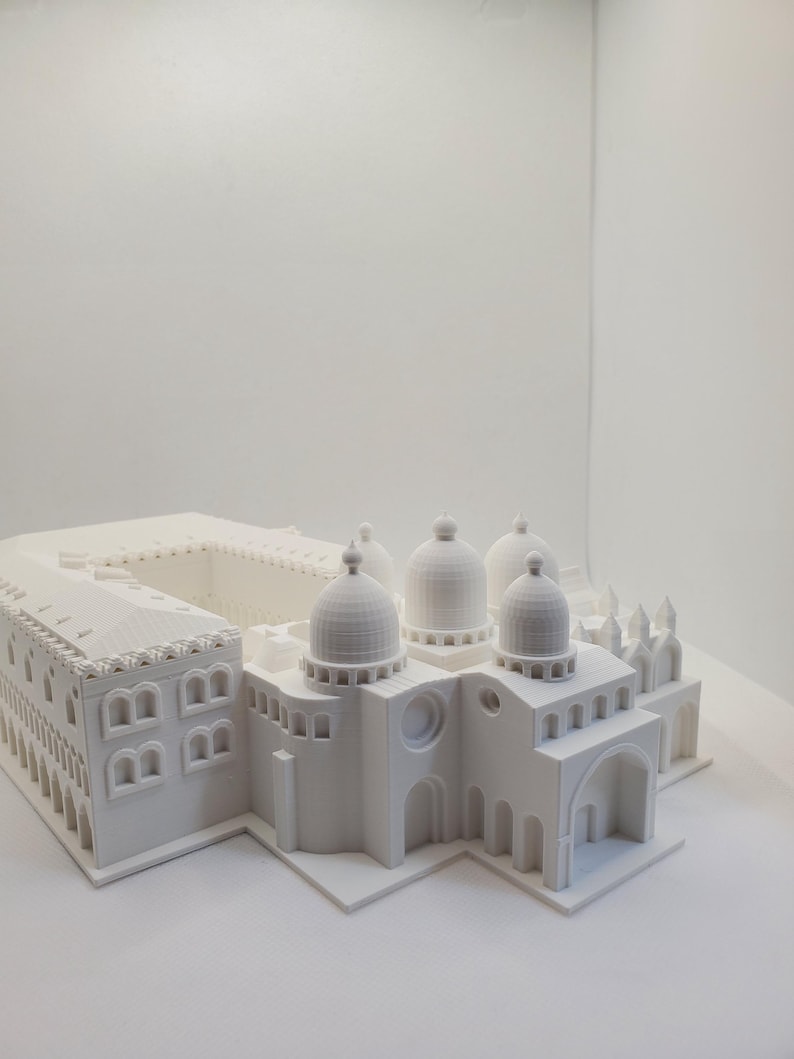 May include: A white 3D printed model of a building with multiple domes and arches. The model is detailed and intricate, with visible windows and other architectural features.