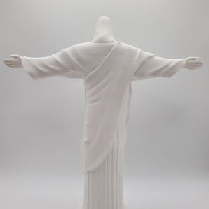 May include: White painted statue of Jesus Christ with outstretched arms, standing on a pedestal.
