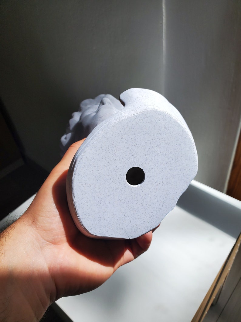 May include: A white ceramic bust sculpture with a textured surface. The bust has a hole in the bottom for drainage.