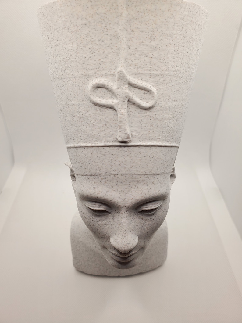 K&ouml;nnte beinhalten: Wei&szlig;e B&uuml;ste eines Menschen, der eine traditionelle &auml;gyptische Kopfbedeckung mit einem Hieroglyphen-Symbol auf der Vorderseite tr&auml;gt. Die Skulptur hat eine strukturierte Oberfl&auml;che.