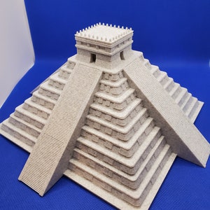 Op de afbeelding: Een beige 3D-geprint model van een Maya-piramide met een vierkante basis en een trapvormige structuur. De piramide heeft een kleine rechthoekige structuur bovenop met een plat dak.
