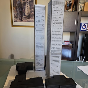 Könnte beinhalten: Ein detailliertes Architekturmodell der Twin Towers mit zwei hohen, grauen Wolkenkratzern mit zahlreichen Fenstern. Das Modell umfasst die schwarzen Basisstrukturen, die auf einer weißen Plattform stehen. Die Darstellung des World Trade Centers.