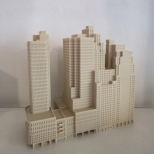 May include: A beige architectural model of a city block featuring multiple high-rise buildings with grid-patterned windows, flat roofs, and tiered levels. The structure is monochromatic and displays a dense urban layout with varying building heights.