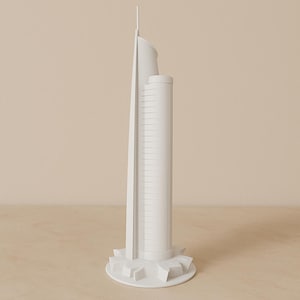 以下が含まれることがあります： 白い近代的な超高層ビルの建築模型。建物は、垂直線のある高い円筒形の塔、湾曲したセクション、尖塔を備えています。模型は、幾何学的な形をした円形の基盤にあります。
