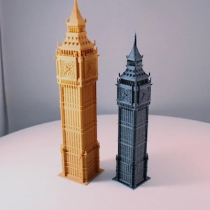 May include: Two 3D printed models of Big Ben, one in gold and one in black. The models are detailed and include the clock faces.