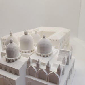 May include: A white 3D printed model of a building with multiple domes and arches. The model is detailed and intricate, with a textured surface.