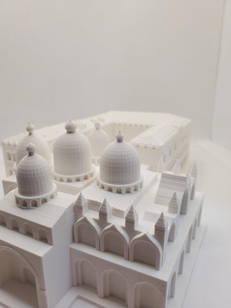 May include: A white 3D printed model of a building with multiple domes and arches. The model is detailed and intricate, with a textured surface.