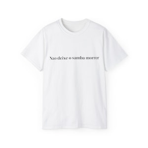 May include: White t-shirt featuring the black text "Nao deixe o samba morrer". The shirt has a crew neck and short sleeves. The phrase is printed centrally on the front of the garment.