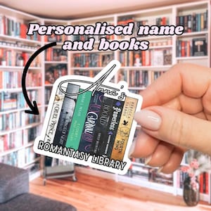 May include: A sticker featuring a stack of books with the text "Romantasy Library." The sticker includes the name "Anna's" and book titles like "Cruel Prince" and "Hooked." The background shows a bookshelf.