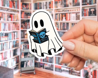 May include: A white ghost sticker with black eyes and a black mouth is reading a book. The book has a blue cover with a skull and the words "LIGHTS OUT". The sticker is held in front of a bookshelf.