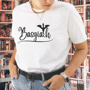 May include: White t-shirt with a black silhouette of a dragon and the text "Basgialh" in a cursive font.