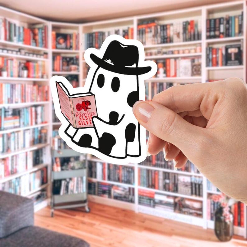 May include: A white sticker featuring a cartoon ghost wearing a black hat and reading a book. The ghost has black spots and is holding a book with the title "Reckless Elsie Silver". The background shows a library.