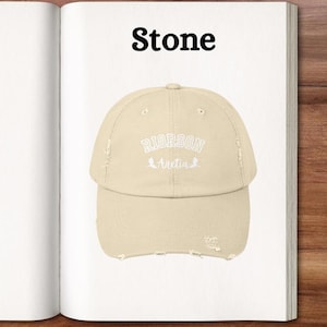 Op de afbeelding: Een baseballpet van steenkleur met een distressed look, met de tekst "RIORSON Avetia" in wit geborduurd.