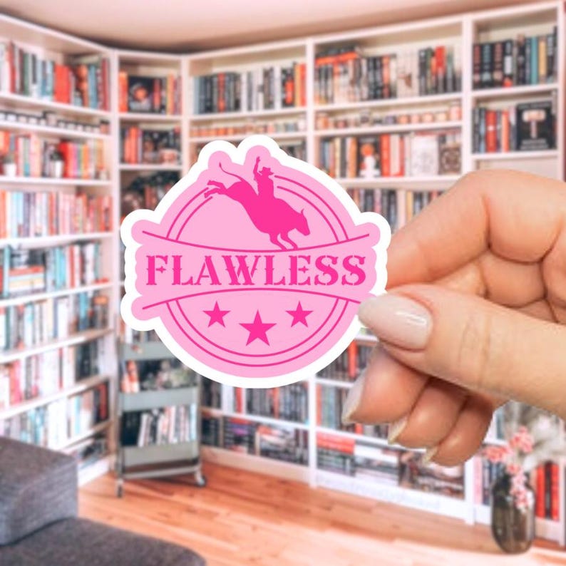 May include: A pink sticker with the word "FLAWLESS" in a circular design. The sticker features a silhouette of a rodeo rider on a bucking bronco, with three stars below the text. The sticker is held in front of a bookshelf.