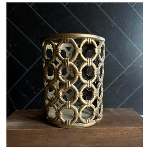 May include: A cylindrical container featuring an openwork design composed of interconnected gold-toned metal rings. The structure has a repeating circular pattern with vertical textured bands at each junction, creating a hollow, cage-like appearance.